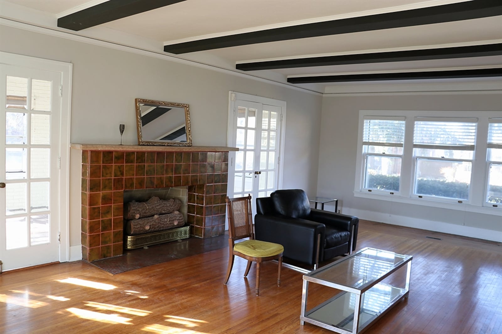 The living room has the same beautiful picture-frame wood flooring with windows to the front and back, filling the room with natural light. Double French doors flank the decorative fireplace, which has polished tile surround and a stone mantel. Painted beams extend across the 10-foot ceiling.