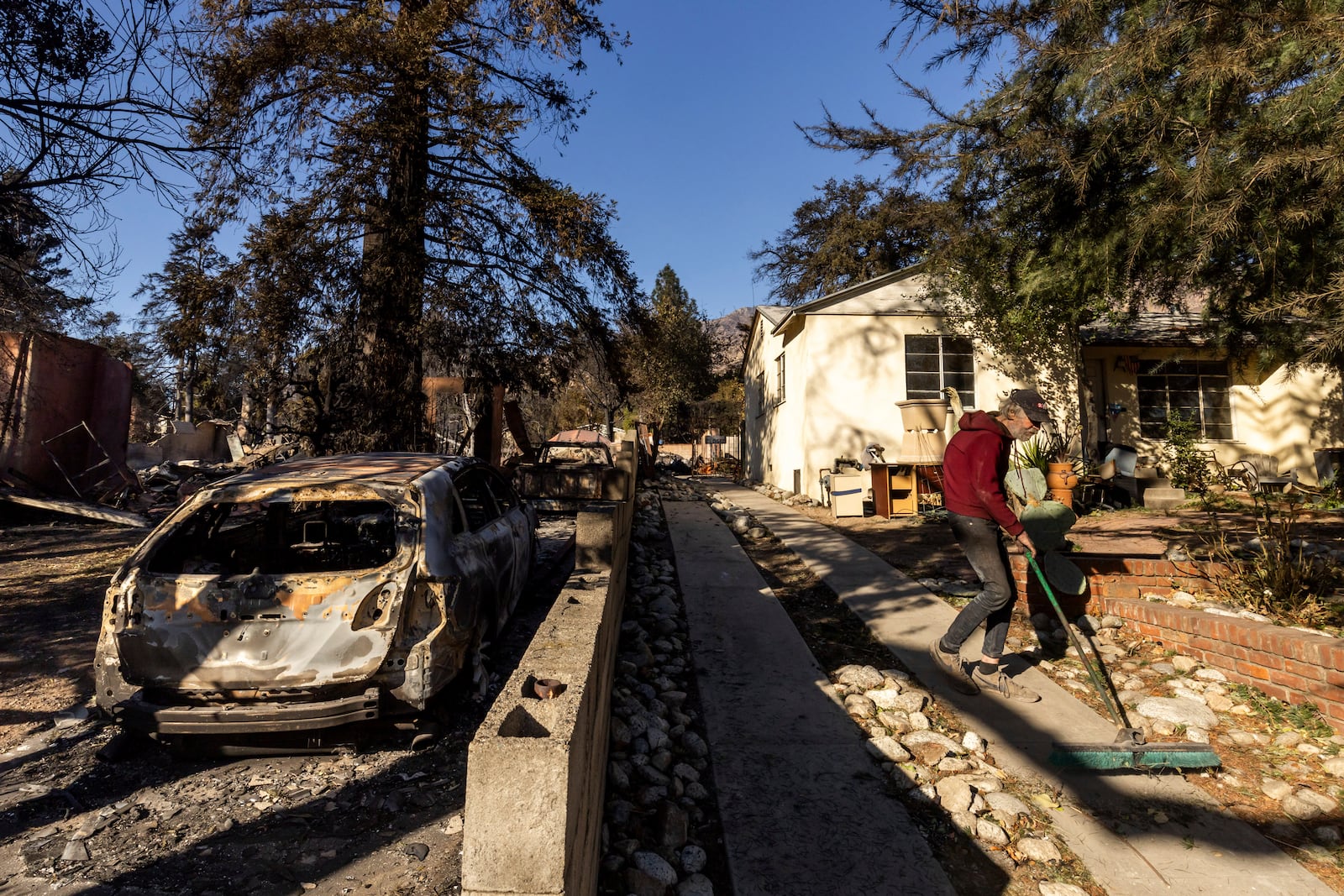 David Slater, right, clears the driveway from his home, spared from the Eaton Fire, Sunday, Jan. 12, 2025 in Altadena, Calif. (AP Photo/Ethan Swope)