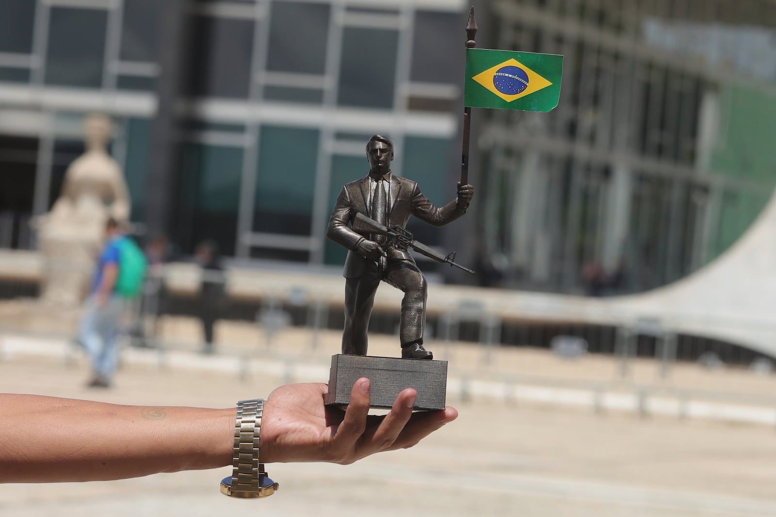 A street vendor shows a sculpture of Brazil's former President Jair Bolsonaro holding a gun and his nation's flag outside the Supreme Court where Bolsonaro is on trial in Brasilia, Brazil, Tuesday, March 25, 2025. (AP Photo/Eraldo Peres)