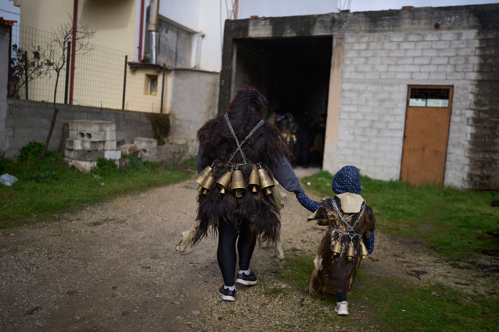 Vasiliki Pergada and her 4-year-old daughter Panagiota, dressed in animal skins and heavy bronze bells, join revelers gathering to take part in carnival celebrations in Distomo, a village in central Greece, on Monday, March 3, 2025. (AP Photo/Petros Giannakouris)