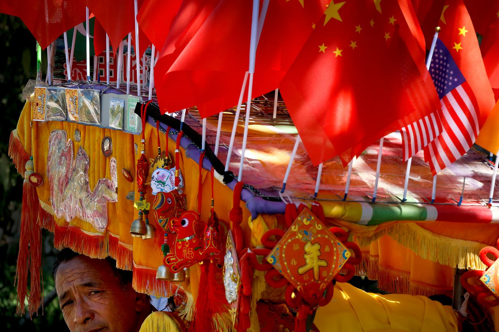 FILE - A driver looks out from his trishaw decorated with an American flag and Chinese flags in Beijing on Sept. 16, 2018. (AP Photo/Andy Wong, File)