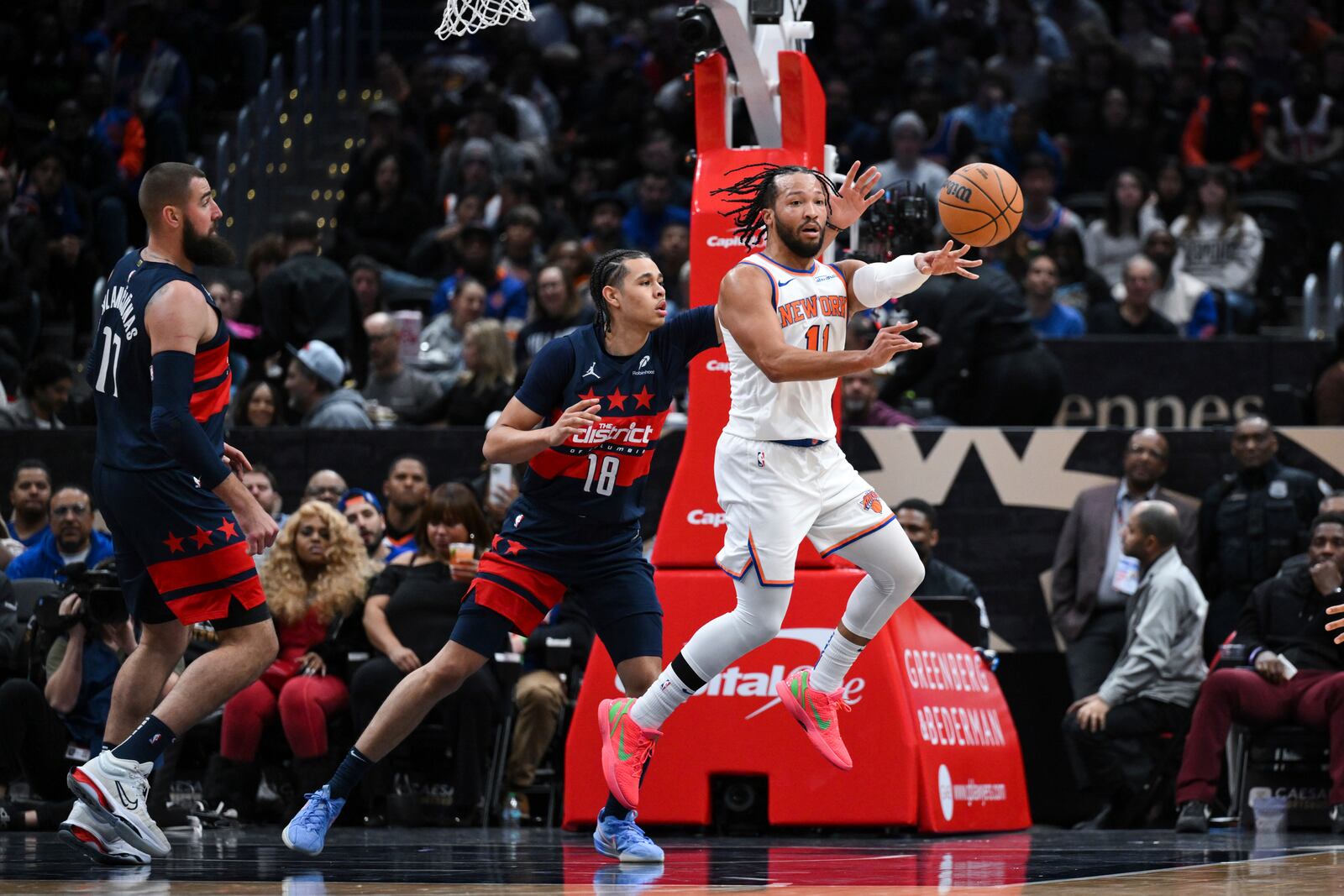 New York Knicks guard Jalen Brunson (11) passes the ball as Washington Wizards forward Kyshawn George (18) defends during the first half of an NBA basketball game, Saturday, Dec. 28, 2024, in Washington. (AP Photo/Terrance Williams)