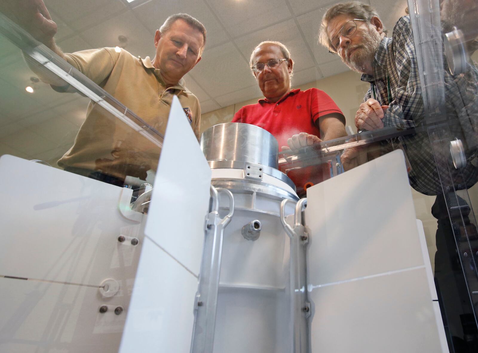 University of Dayton Research Institute scientists and engineers Chadwick Barklay, left, Daniel Kramer and Richard Harris observe a Multi-Mission Radioisotope Thermoelectric Generator that converts the heat from the natural decay of a plutonium-238 dioxide to electricity through solid-state thermoelectric couples.  TY GREENLEES / STAFF