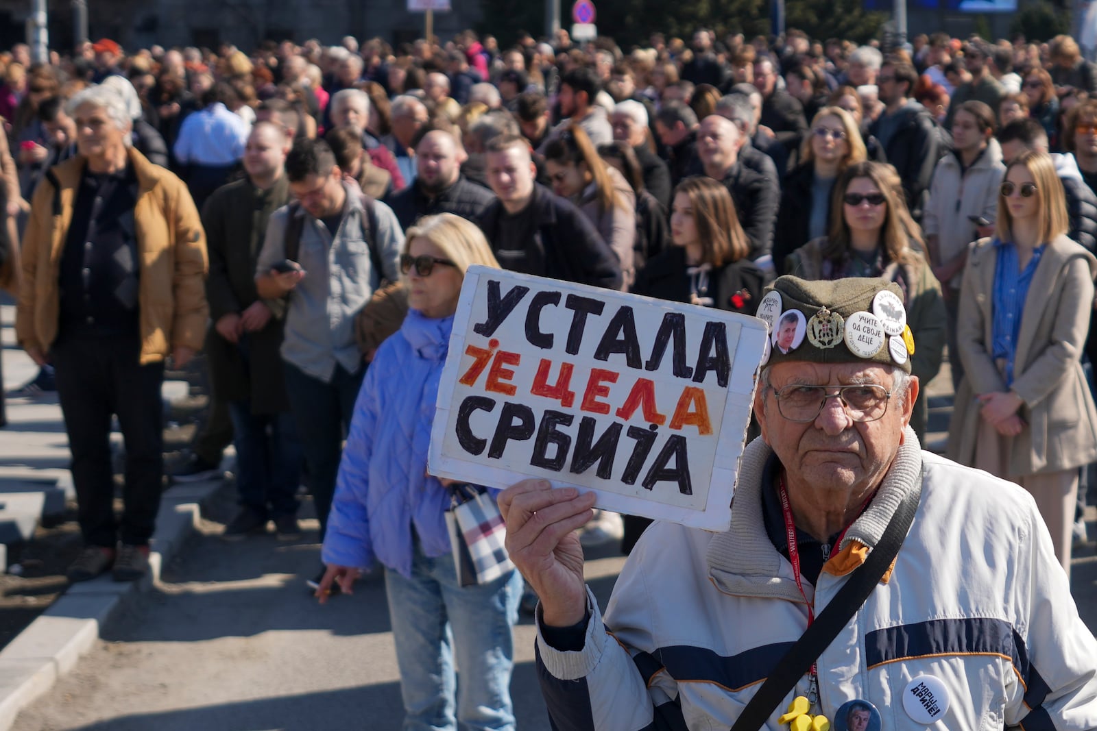 A man holds a banner reading: "All of Serbia has risen" and stands in silence to commemorate the 15 victims killed after a railway concrete canopy fell in November 2024, during a Serbia's parliament session in Belgrade, Serbia, Tuesday, March 4, 2025. (AP Photo/Darko Vojinovic)