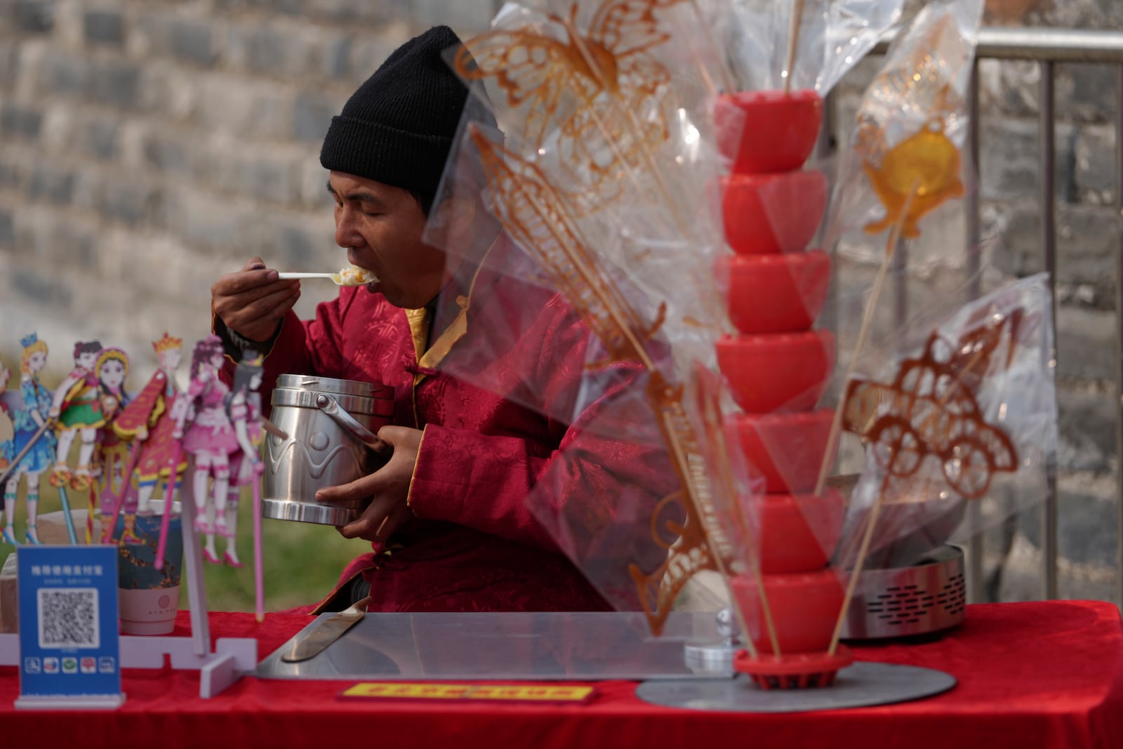 A vendor eats lunch at his store selling traditional sugar sculptures while waiting for customer at the Chongwenmen Gate in Beijing, Sunday, March 9, 2025. (AP Photo/Andy Wong)