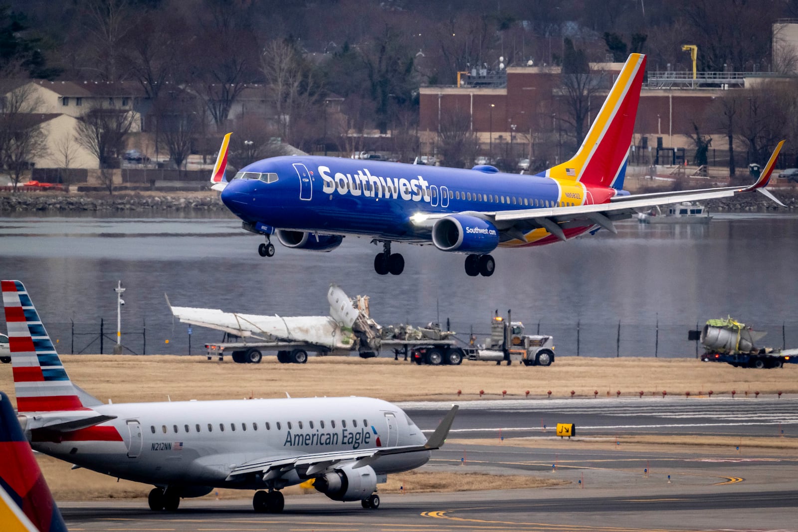 Aircraft land next to flatbed trucks carrying pieces of wreckage, near the site in the Potomac River of a mid-air collision between an American Airlines jet and a Black Hawk helicopter, at Ronald Reagan Washington National Airport, Wednesday, Feb. 5, 2025, in Arlington, Va. (AP Photo/Ben Curtis)