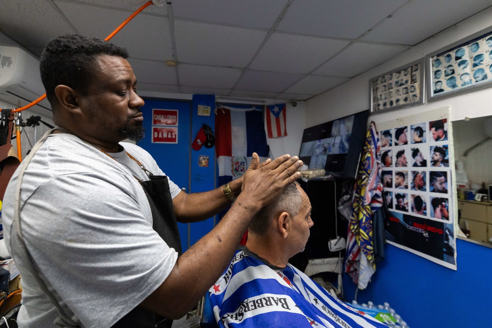 Ricardo Perez, a Dominican barber who's lived in Puerto Rico for over 20 years, explains how his business has seen a drop in sales since raids on immigrant communities began during the second Trump administration, while giving a haircut in San Juan, Puerto Rico, Friday, March 14, 2025. (AP Photo/Alejandro Granadillo)