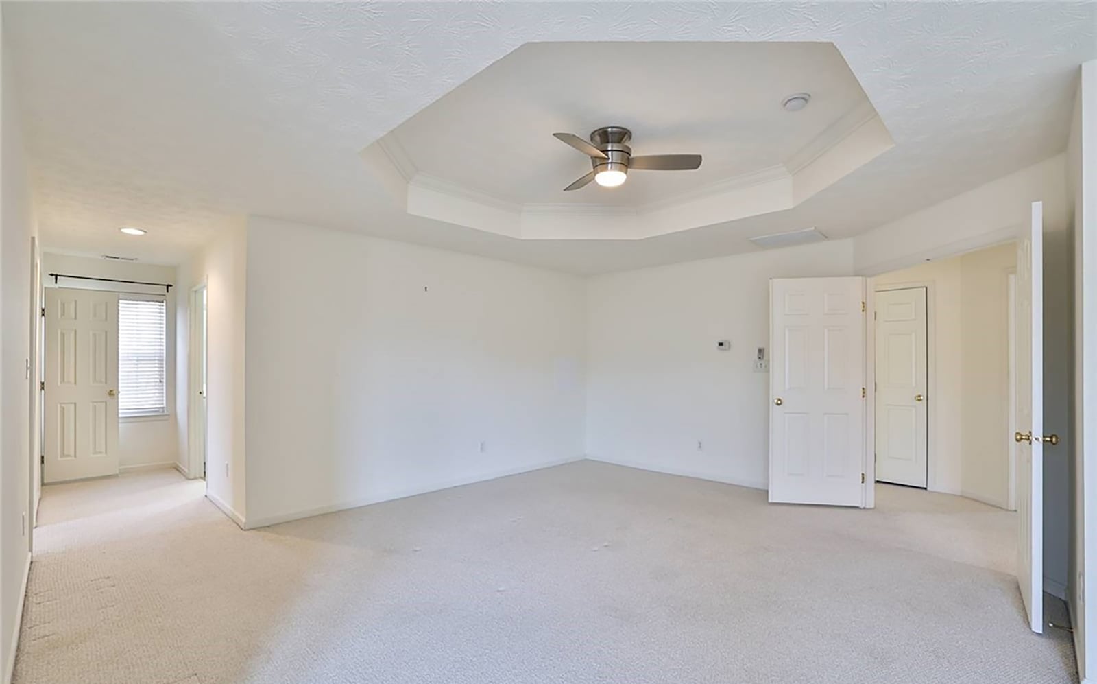 The primary bedroom suite has neutral carpeting and a trey ceiling with ceiling fan. There is ample walk in closet space and an ensuite bathroom with separate garden tub.