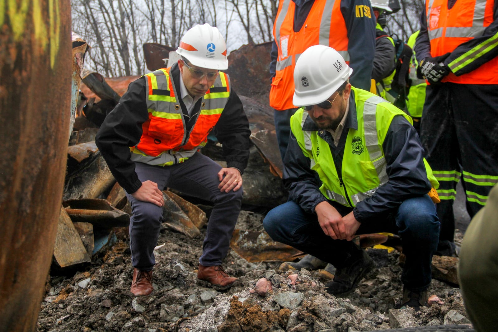 Transportation Secretary Pete Buttigieg, left, and Tristan Brown, deputy administrator of the Pipeline and Hazardous Materials Safety Administration, crouch down to look at part of a burned traincar, Thursday, Feb. 23, 2023, in East Palestine, Ohio, at the site of a Norfolk Southern train derailment. (Allie Vugrincic/The Vindicator via AP, Pool)