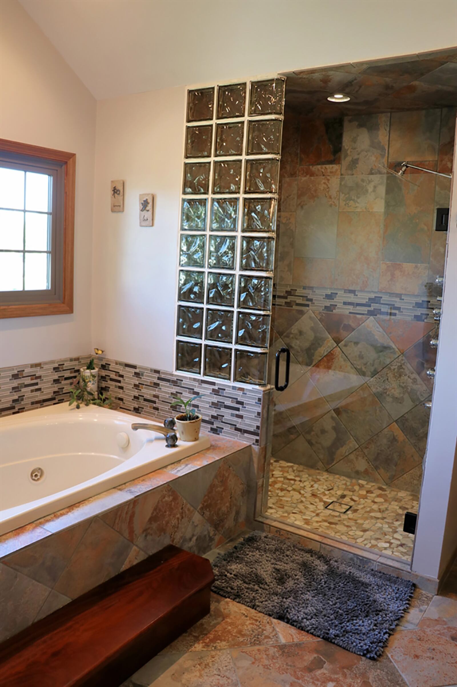 The main suite’s bathroom has been updated with a whirlpool tub below a window and a cathedral ceiling. The walk-in shower has several shower heads and jetted body wash with ceramic-tile, glass-block and river-rock accents and heated-tile flooring. CONTRIBUTED PHOTO BY KATHY TYLER