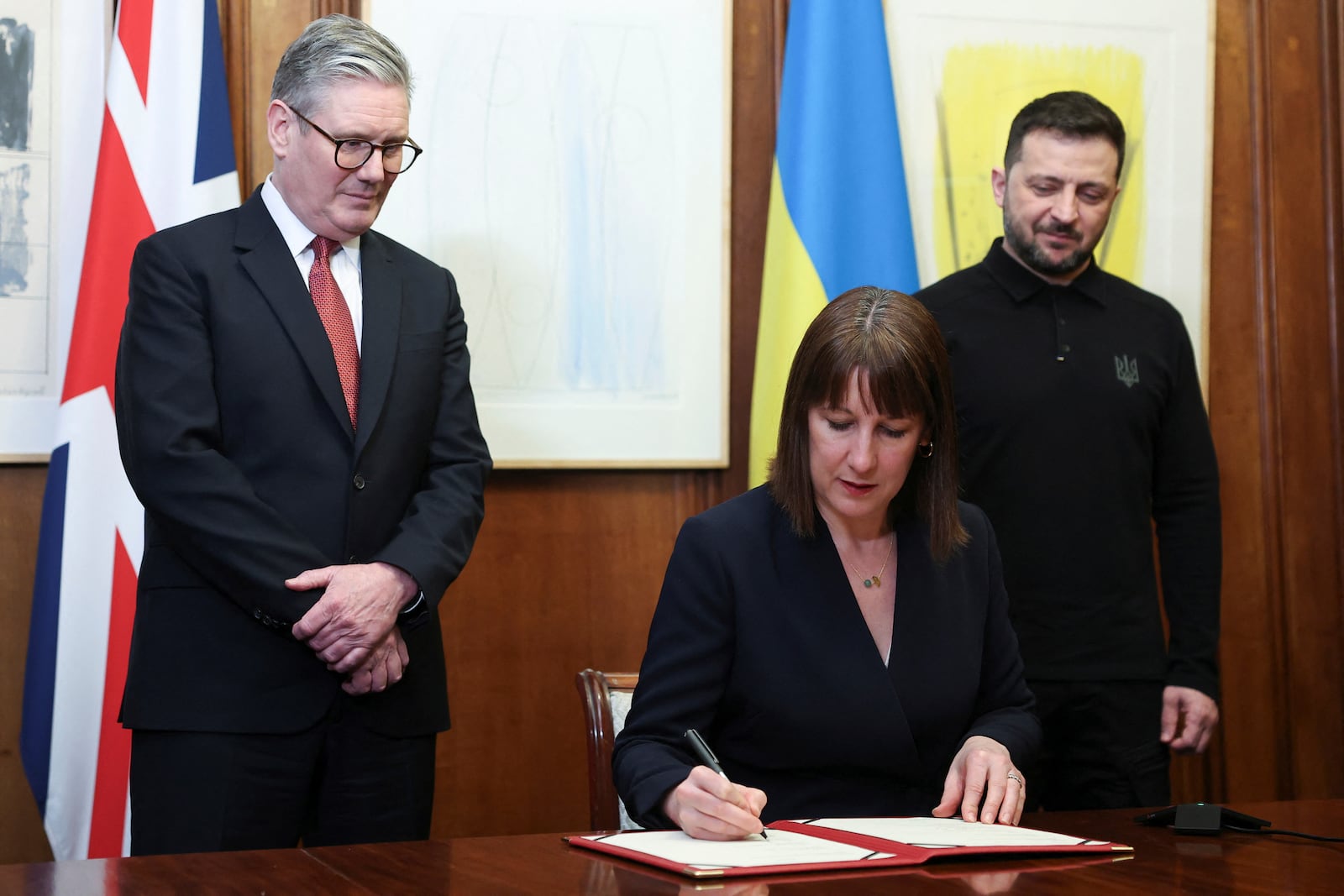 Britain's Chancellor of the Exchequer Rachel Reeves, front, signs a document of defence lend for Ukraine on the day she holds a video conference meeting with Ukraine's Finance Minister Sergii Marchenko, as British Prime Minister Keir Starmer, left, and Ukrainian President Volodymyr Zelenskiyy, right, stand in London, England, March 1, 2025. (Toby Melville/Pool Photo via AP)