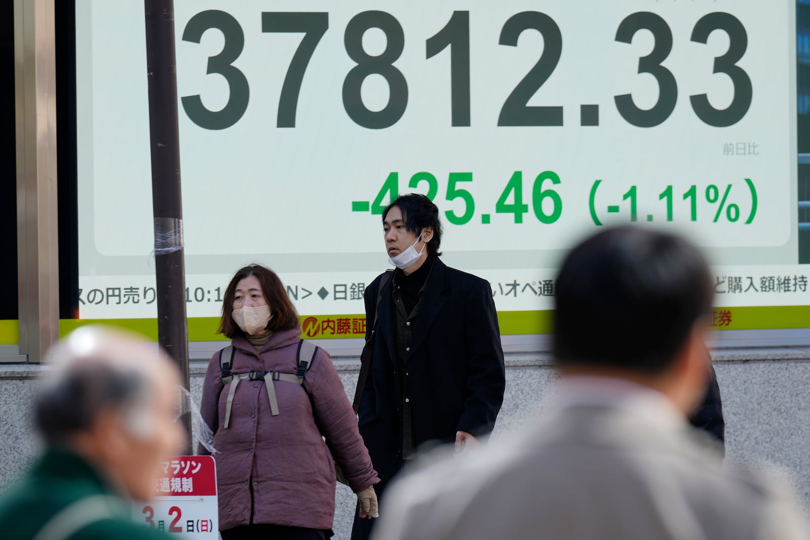 Persons walk past an electronic stock board showing Japan's Nikkei index at a securities firm Wednesday, Feb. 26, 2025, in Tokyo. (AP Photo/Eugene Hoshiko)