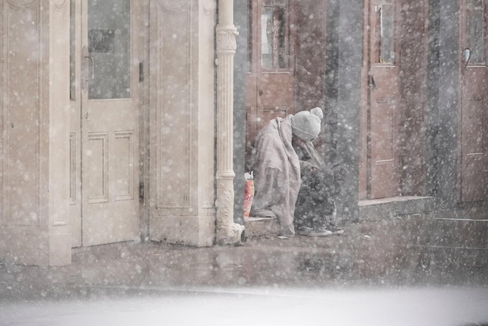 A homeless man sits in a doorway as snow falls in the French Quarter in New Orleans, Tuesday, Jan. 21, 2025. (AP Photo/Gerald Herbert)