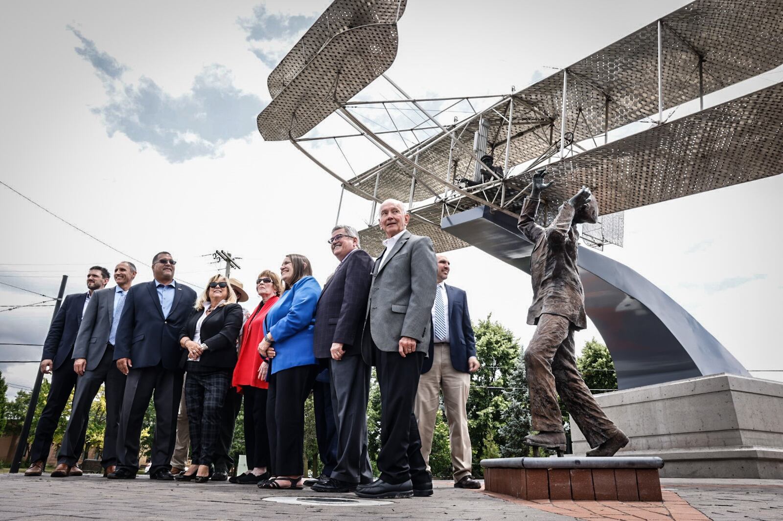 City of Dayton officials pose for pictures in front of the Wright Flyer III sculpture following the ribbon cutting ceremony at the intersection of Edwin C. Moses and West Third Street Wednesday 14, 2023. The sculpture was moved from Monument Avenue after a developer bought the land. JIM NOELKER/STAFF