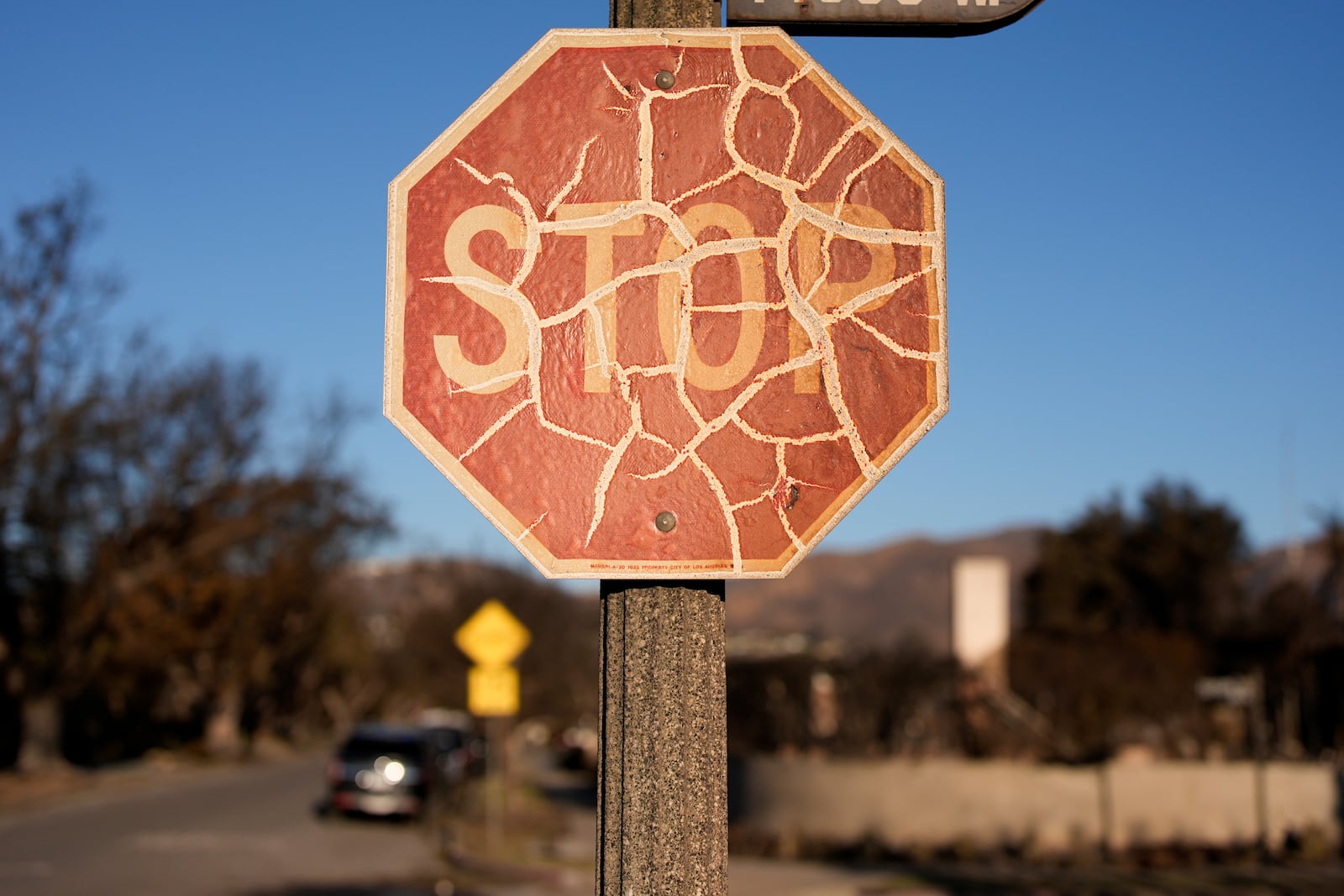 A stop sign is damaged in the aftermath of the Palisades Fire in the Pacific Palisades neighborhood of Los Angeles, Monday, Jan. 13, 2025. (AP Photo/John Locher)