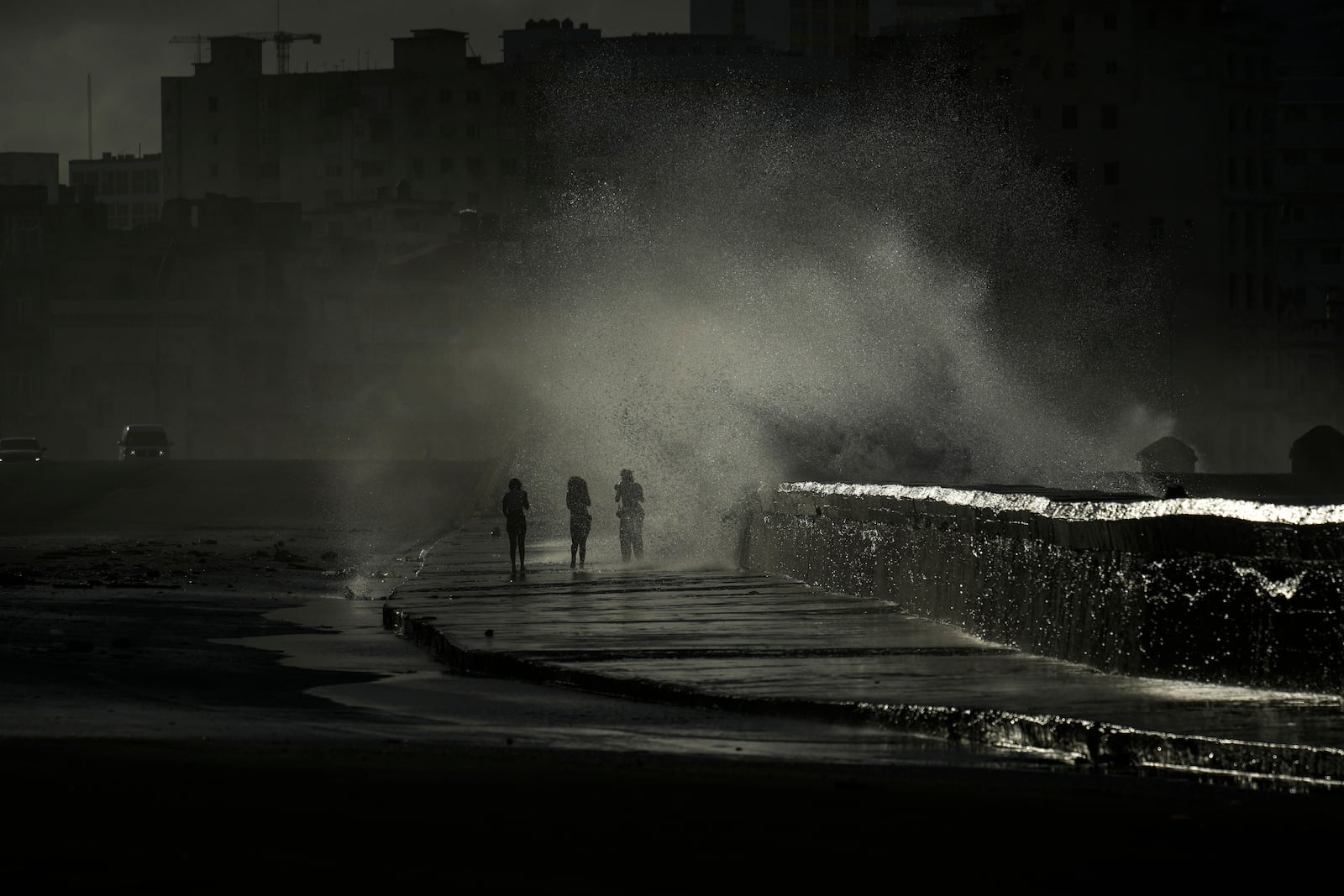 People walk along the boardwalk as waves crash in Havana, Monday, Oct. 21, 2024. (AP Photo/Ramon Espinosa)