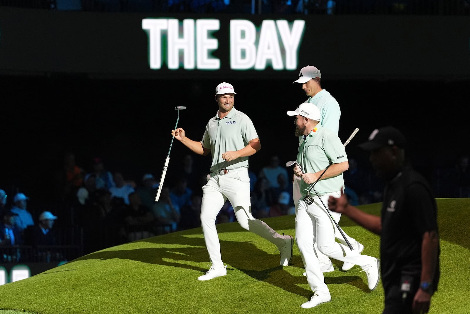 The Bay Golf Club's Wyndham Clark, left, and teammates Ludvig Aberg, top, and Shane Lowry celebrate winning the third hole during the inaugural match of the TMRW Golf League, Tuesday, Jan. 7, 2025, in Palm Beach Gardens, Fla. TGL features six teams of four players competing against each other in a tech-infused arena the size of a football field. (AP Photo/Rebecca Blackwell)