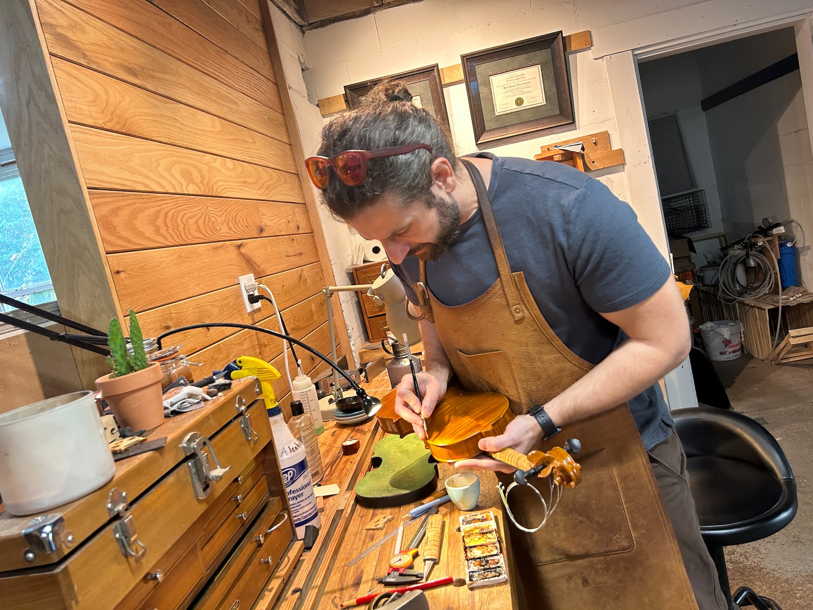 Luthier Joel Thompson in his workshop, Side Door Strings. A luthier is a craftsperson who builds and repairs stringed instruments that are played with a bow or plucked. Here Thompson is mixing varnish tints and touching up a violin.