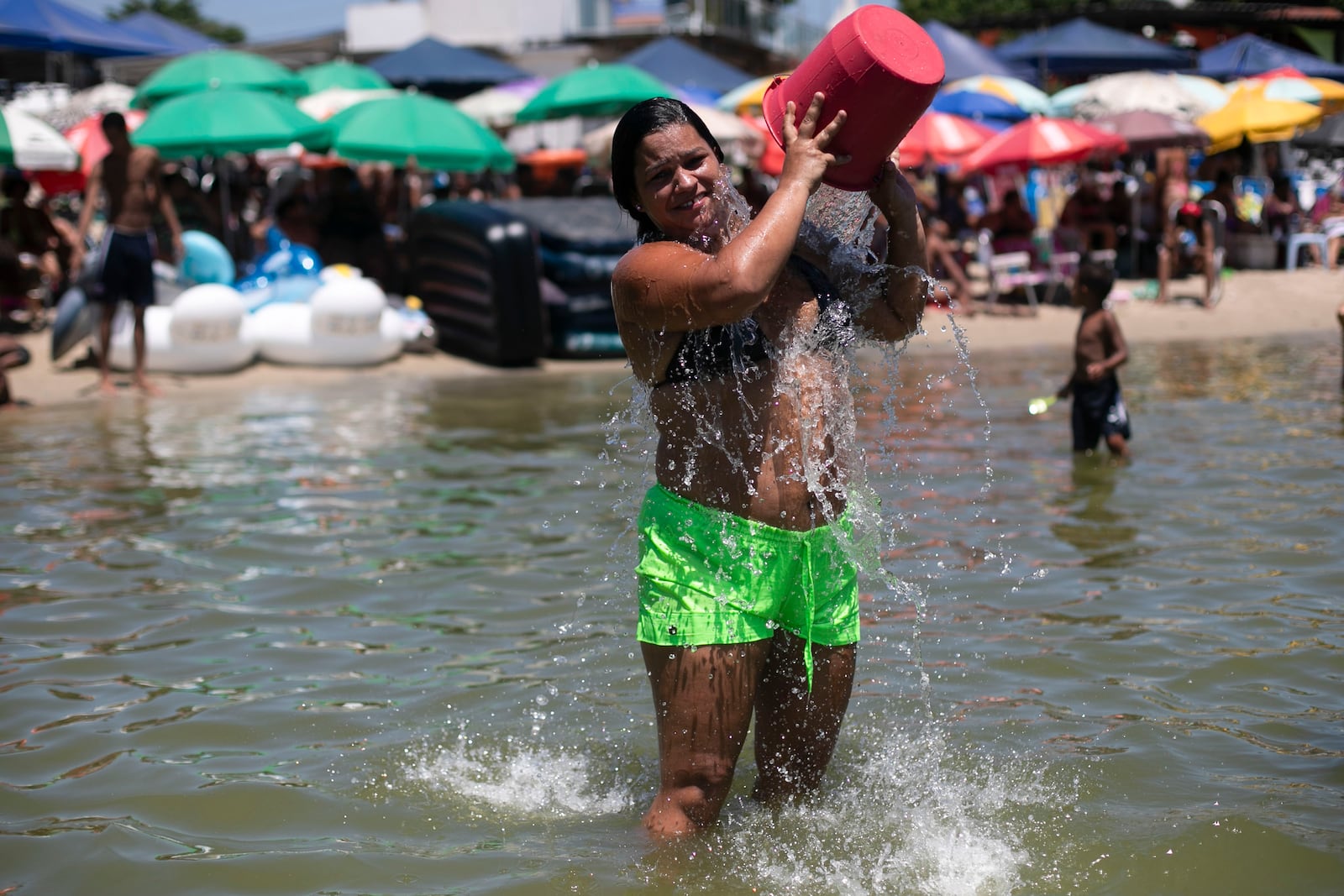 A woman cools herself off with a bucket of water at the Piscinao de Ramos artificial beach during summer in Rio de Janeiro, Sunday, Feb. 16, 2025. (AP Photo/Bruna Prado)