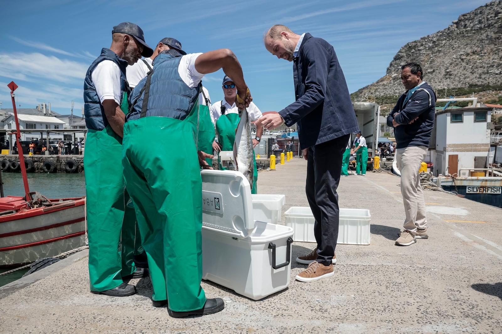 Britain's Prince William, the Prince of Wales is handed a fish as he speaks to local fisherman, at Kalk Bay Harbour, near Cape Town, Thursday, Nov. 7, 2024. (Gianluigi Guercia/Pool Photo via AP)