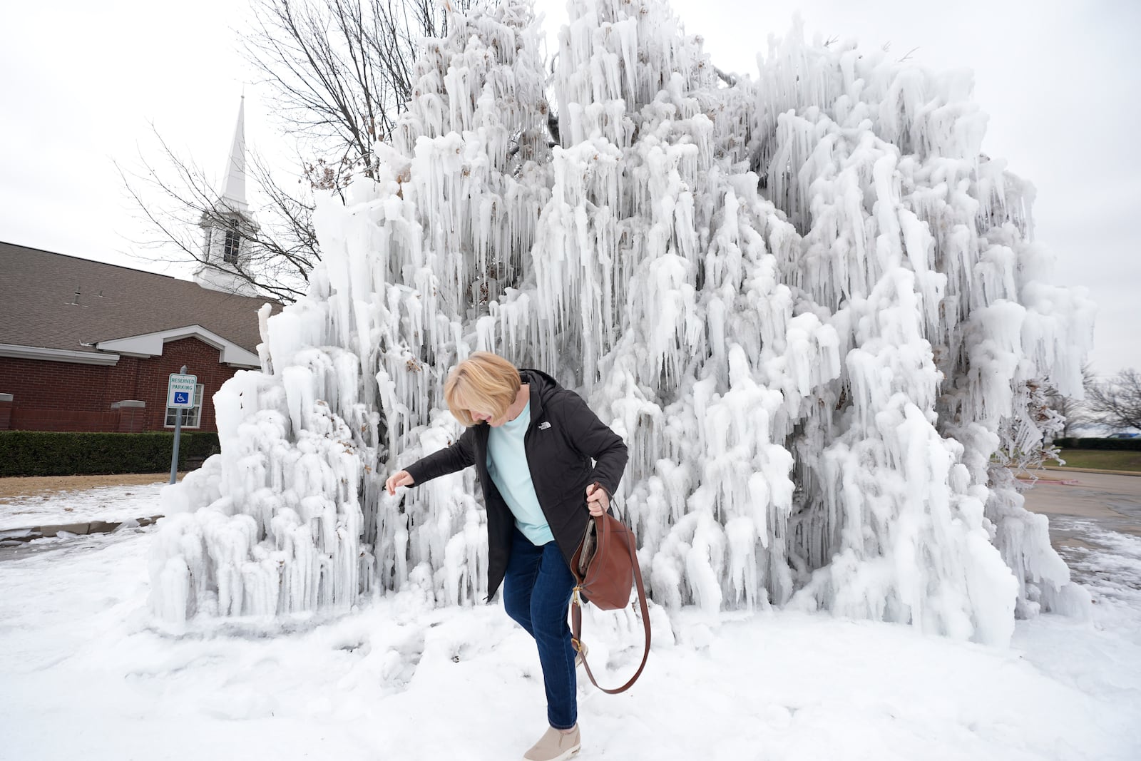 Linda Johnson carefully walks on ice caused by a water main break and cold winter temperatures outside her church in Frisco, Texas, Friday, Feb. 21, 2025. (AP Photo/LM Otero)