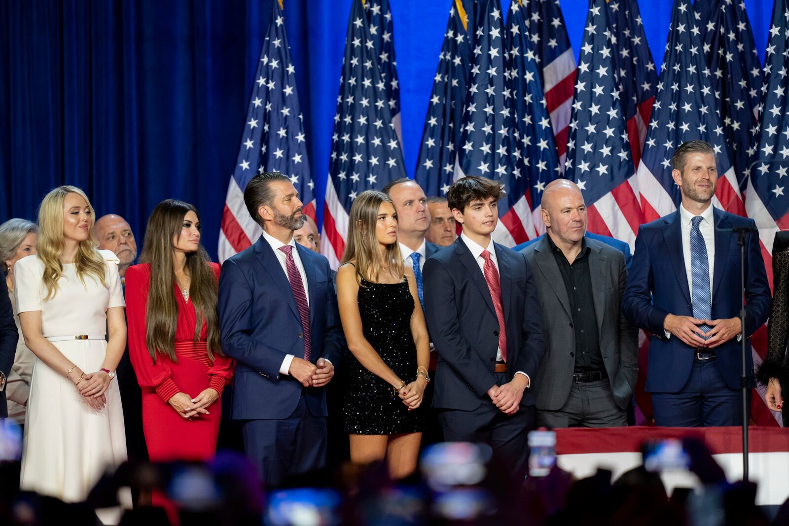 From left, Susie Wiles, Tiffany Trump, Tony Fabrizio, Kimberly Guilfoyle, Donald Trump Jr., Walt Nauta (hidden two people), Kai Madison Trump, Dan Scavino, Corey Lewandowski, Donald Trump III, Dana White, Chris LaCivita and Eric Trump, listen as Republican presidential nominee former President Donald Trump speaks at an election night watch party Wednesday, Nov. 6, 2024, in West Palm Beach, Fla. (AP Photo/Alex Brandon)