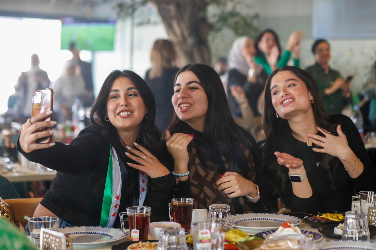 FILE - A Syrian woman with a scarf in colors of the Syrian opposition flag takes a selfie with her friends as they celebrate in a restaurant in Damascus, Syria, Tuesday, Dec. 17, 2024. (AP Photo/Omar Sanadiki, File)