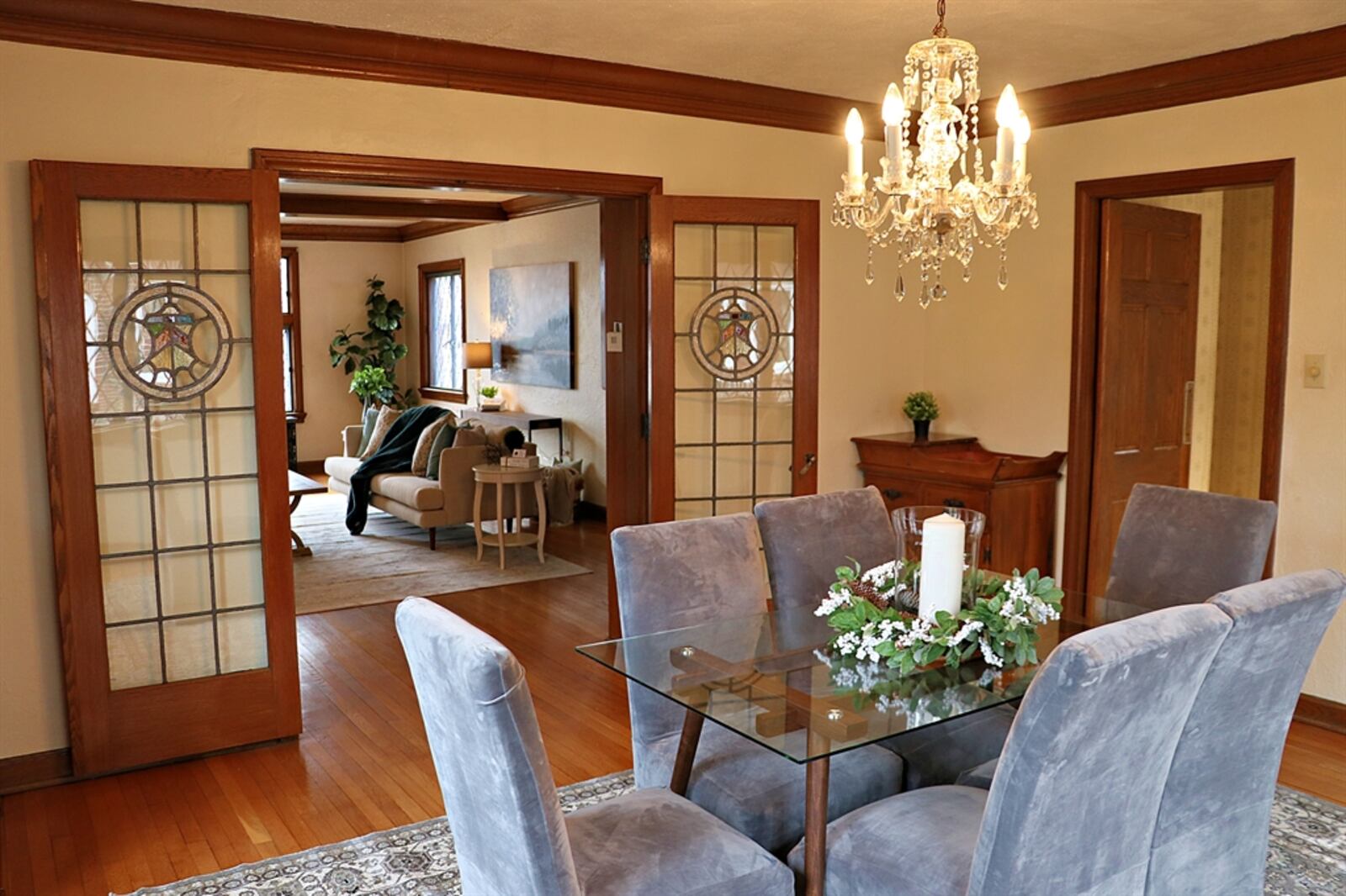 French doors with stained-glass accents open into a formal dining room, which has hardwood flooring. Crown molding frames the crystal chandelier. 