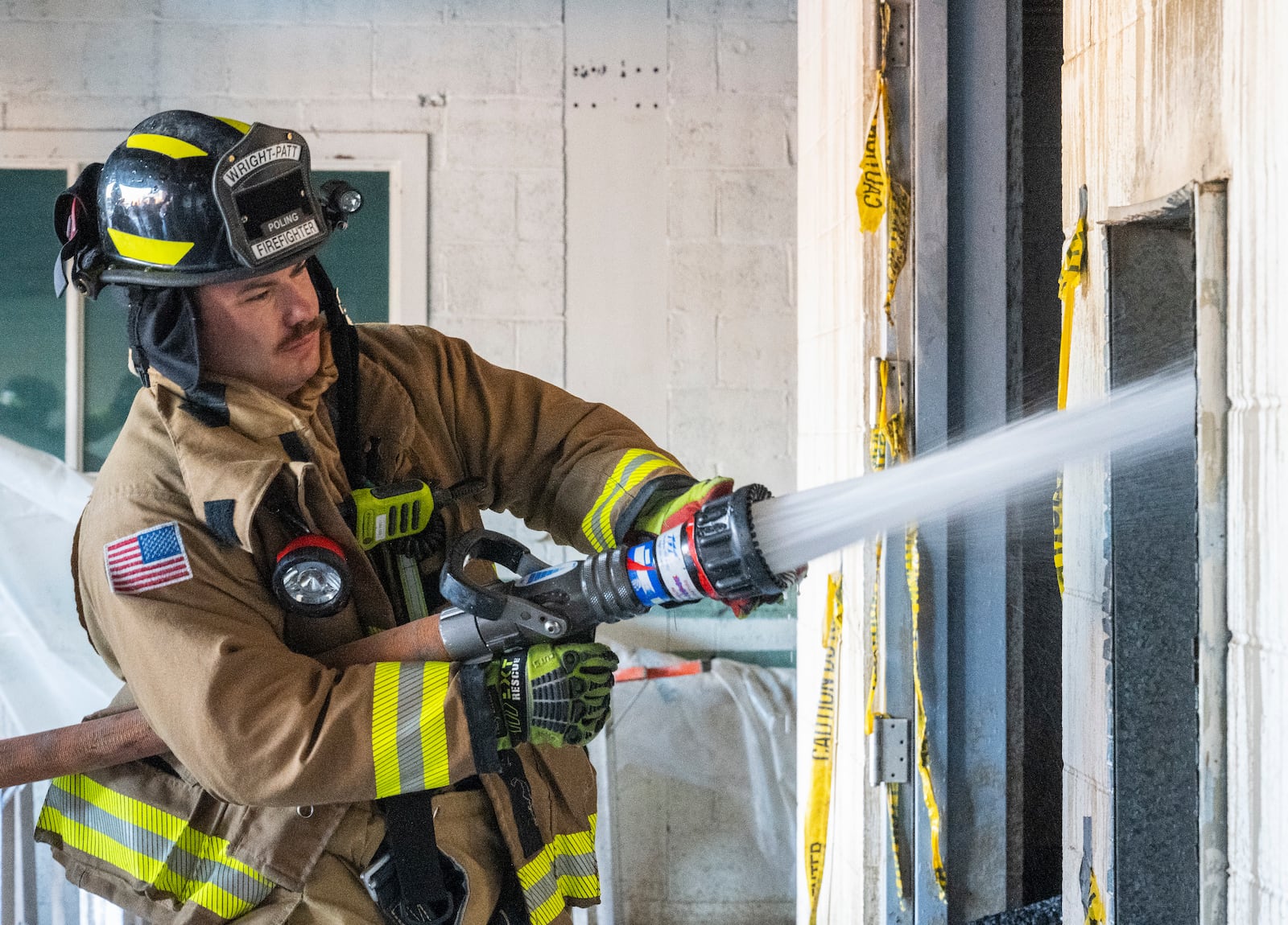 Firefighter Dorian Poling, 788th Civil Engineer Squadron Fire Department, hoses down the wall and ceiling of a room that had been on fire in Building 18, Area B, July 18, at Wright-Patterson Air Force Base. The construction of the walls, timbers sandwiched between steel plates and cement blocks, made it difficult to completely extinguish the embers and caused the fire to reignite the next morning. (U.S. Air Force photo by R.J. Oriez)