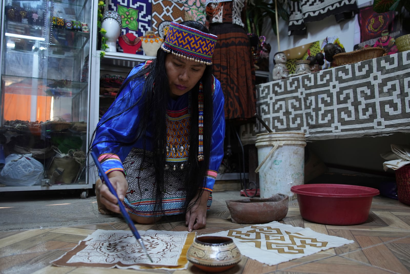 Sadith Silvano, from Paoyhan, a Shipibo-Konibo Indigenous community in the Amazon, paints a tablecloth at her home and workshop in Lima, Peru, Saturday, Oct. 19, 2024. Handpainted textiles like the ones she crafts, known as “kené,” have slowly gained recognition and were declared part of the “Cultural Heritage of the Nation” by the Peruvian government in 2008. (AP Photo/Guadalupe Pardo)