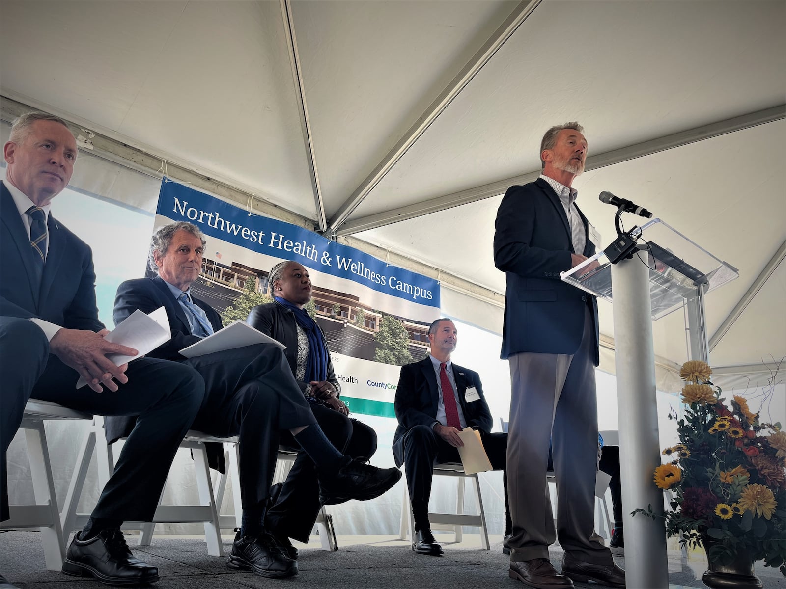 Speakers at a ceremonial groundbreaking on Friday, Oct. 28, 2022, for a new $17.8 million facility on the former Good Samaritan Hospital site in northwest Dayton. At the podium is Gary Blake, past chair of the YMCA of Greater Dayton’s board of directors. Seated are Michael Riordan, president and CEO of Premier Health; U.S. Sen. Sherrod Brown, D-Ohio; Eloise Broner, chief of shared services with Premier; and Dale Brunner, president and CEO of the YMCA of Greater Dayton. CORNELIUS FROLIK / STAFF