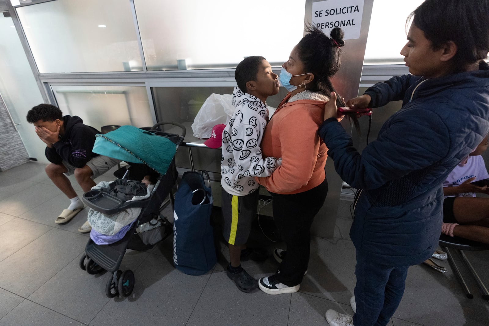 Margelis Rodriguez, second from right, of Venezuela, gets a hug from her son Mickel, 12, as her friend Ale combs her hair as they wait for their laundry at a laundromat near the migrant shelter where the family is staying in Tijuana, Mexico, Friday, Jan. 31, 2025. (AP Photo/Gregory Bull)