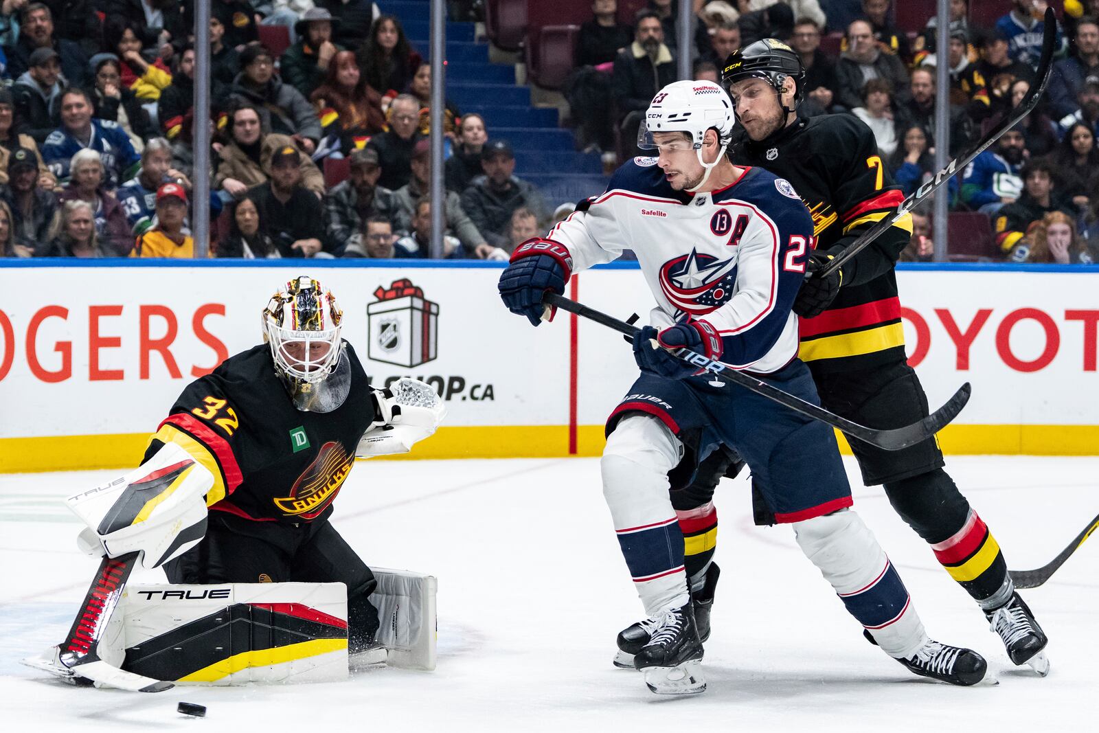 Vancouver Canucks goaltender Kevin Lankinen (32) stops Columbus Blue Jackets' Sean Monahan (23) as Vancouver's Carson Soucy (7) watches during the second period of an NHL hockey game in Vancouver, British Columbia, Friday, Dec. 6, 2024. (Ethan Cairns/The Canadian Press via AP)