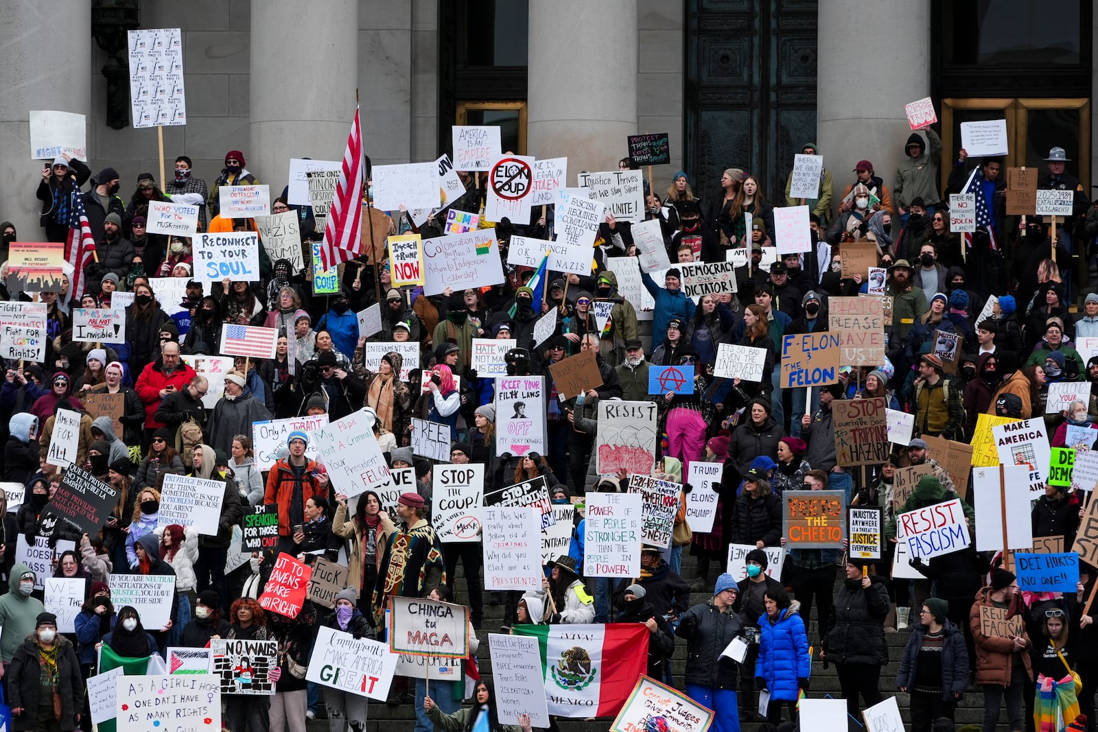 People wave signs as they gather to protest against the Trump administration on the steps of the Washington State Capitol building Wednesday, Feb. 5, 2025, in Olympia, Wash. (AP Photo/Lindsey Wasson)