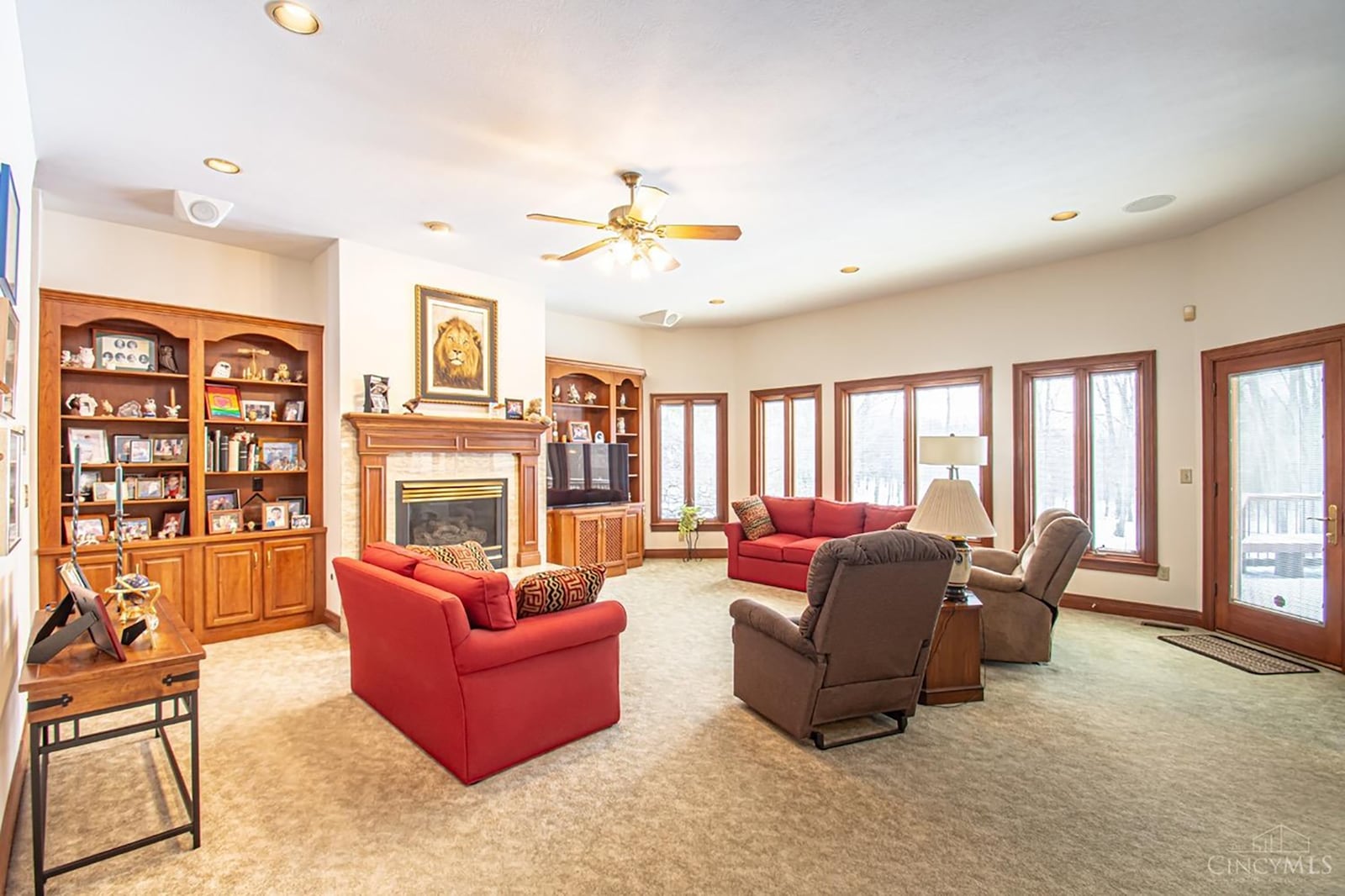 The great room has carpeting, a ceiling fan and two built in bookcases flanking the gas fireplace.