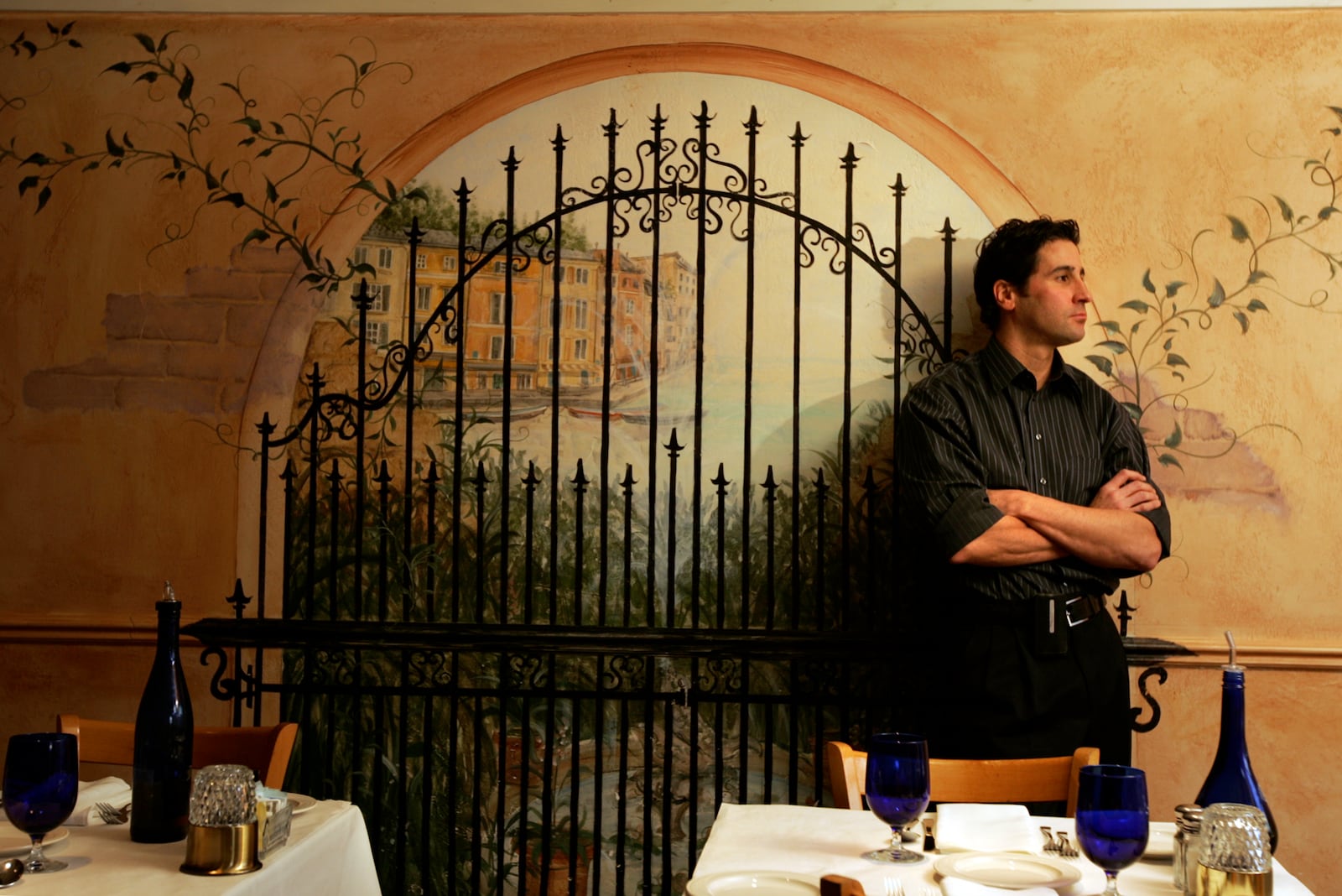 Owner Michael Anticoli looks out a window in his downtown Troy restaurant La Piazza as he stands in front of a faux wall painting in one of the dining areas.