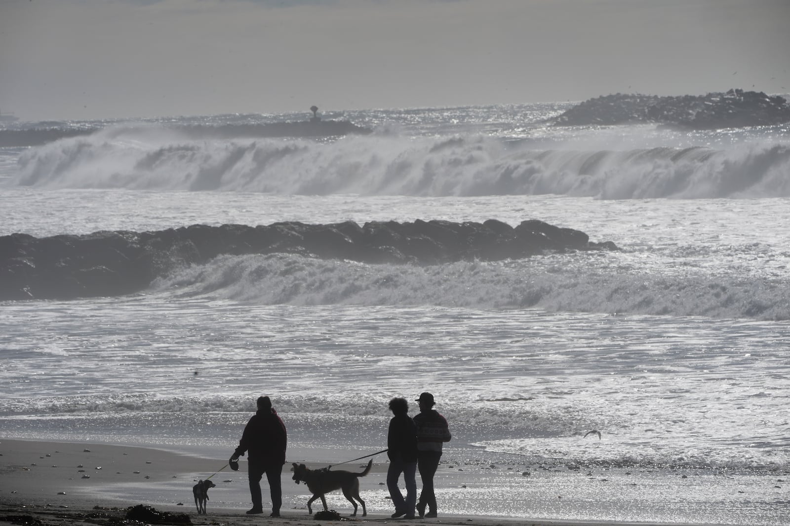 Visitors walk along the beach as high surf comes in Ventura, Calif., Tuesday, Dec. 24, 2024. (AP Photo/Damian Dovarganes)