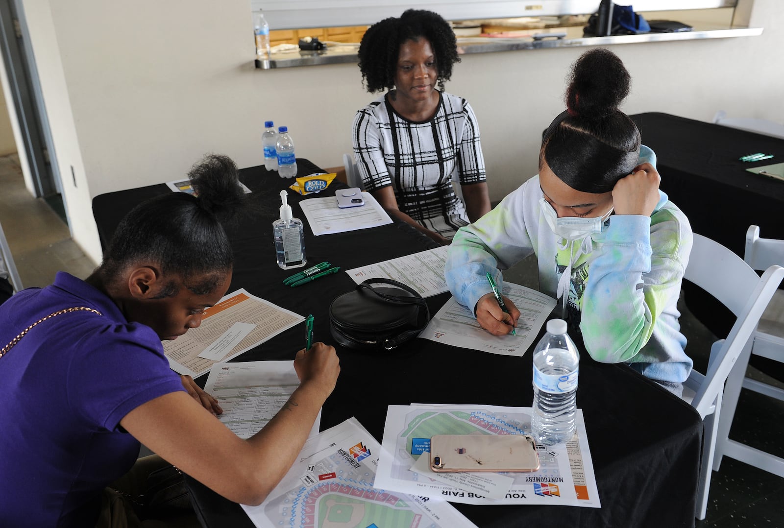 Shada Bennett, an employee of Youth Works watches as Kentaiya Wilder, 17, left and Alyssah Campbell, 17, fill out registration forms at the Day Air Ballpark job fair for young adults Wednesday, May 11, 2022. The event was hosted by the Montgomery County Workforce Development Services. MARSHALL GORBY\STAFF