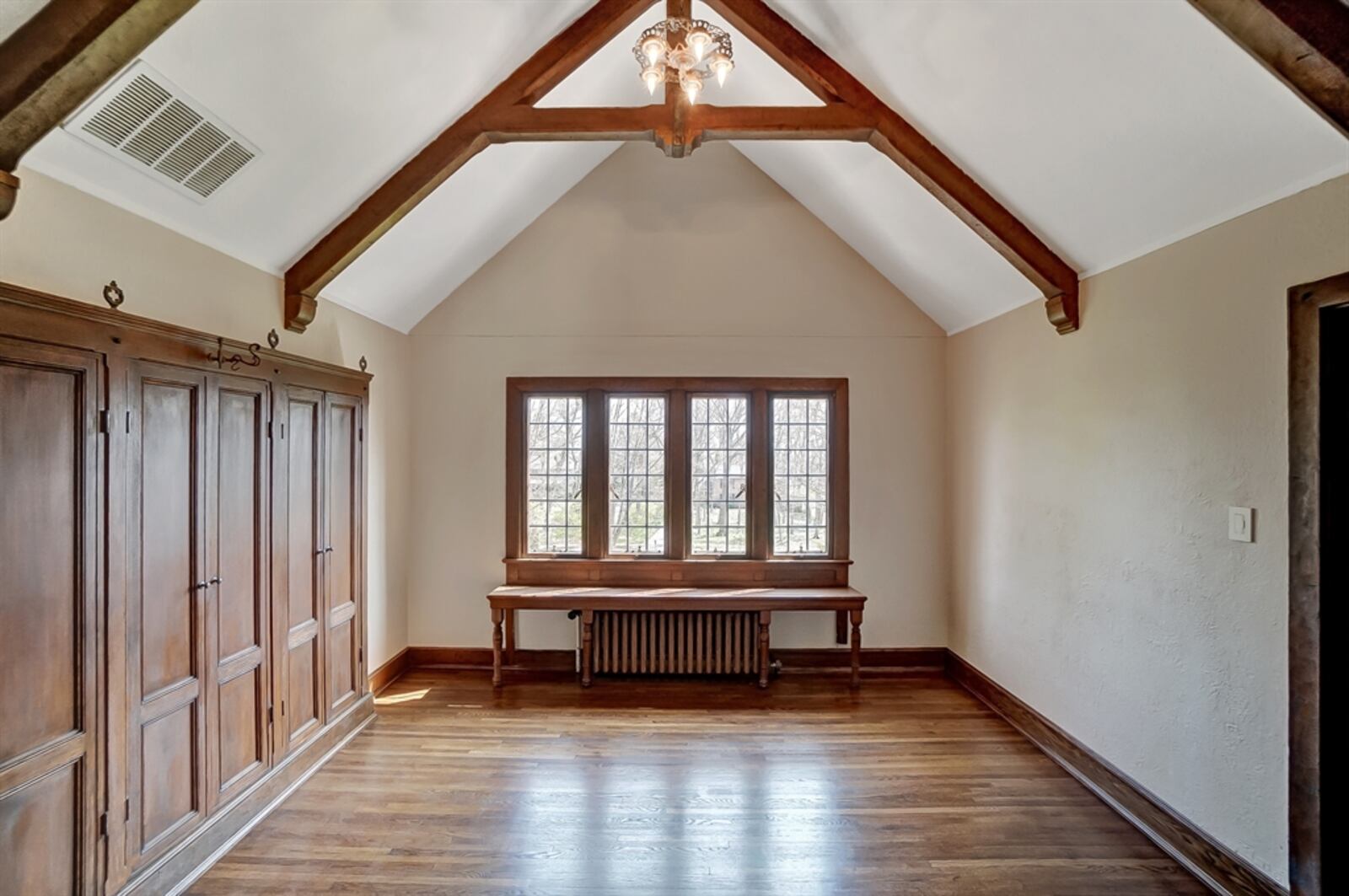 Another room has a cathedral ceiling with raised-tiled king post ceiling beams and a wall with a built-in armoire. This bedroom shares a Jack-and-Jill bathroom with an oversized pedestal sink and a ceramic-surround step-in shower.