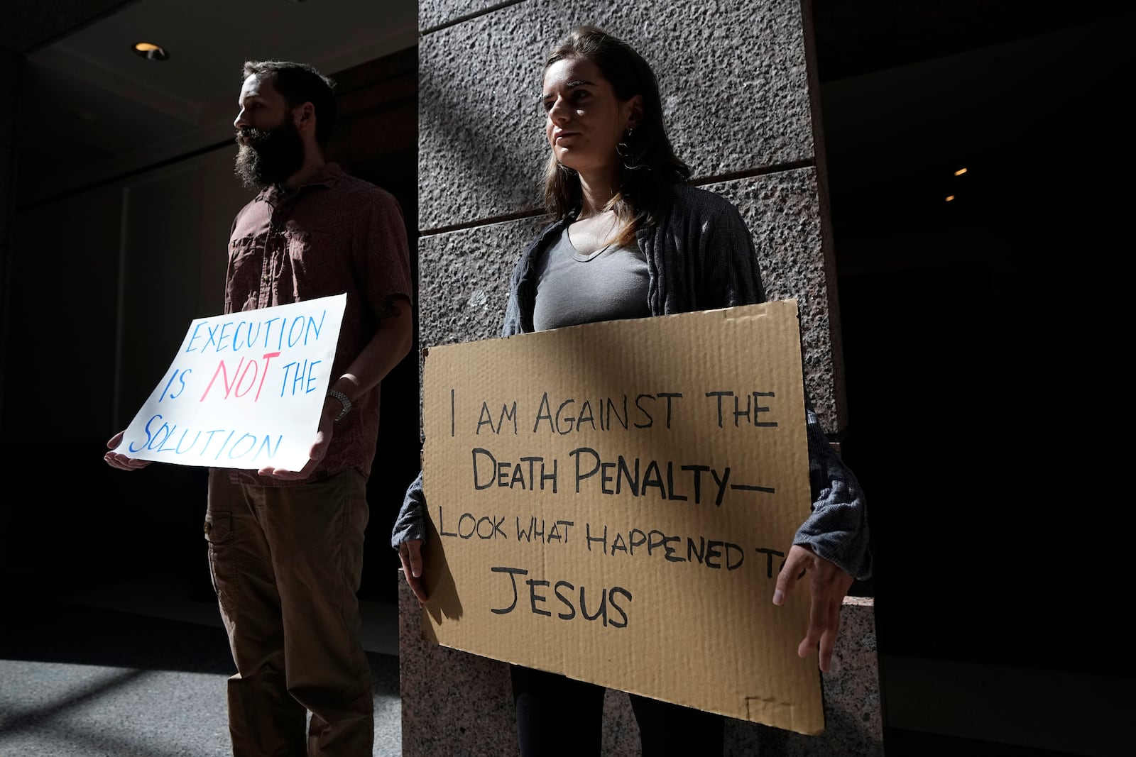 Barrett Hess, left, and Marcella Marino, right, hold signs as they stand outside a room where a committee is discussing the case of death row inmate Robert Roberson, Monday, Oct. 21, 2024, in Austin, Texas. (AP Photo/Tony Gutierrez)