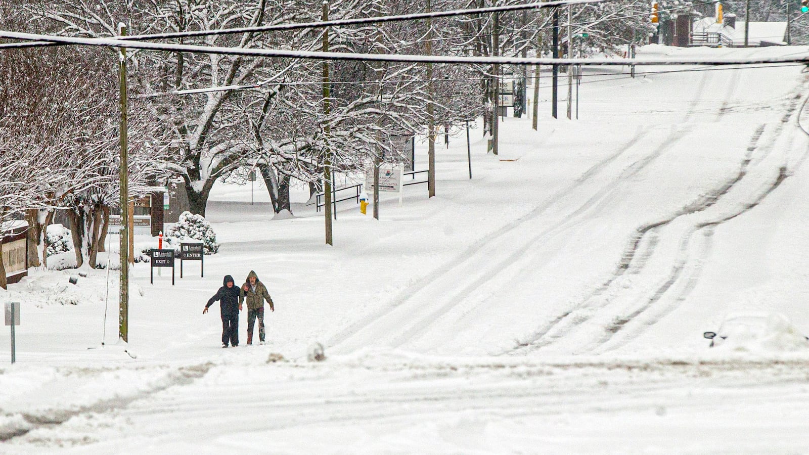 Two people hang onto one another for support while walking along a snow-covered East College Street Friday, Jan. 10, 2025, in Florence, Ala. (Dan Busey/The TimesDaily via AP)