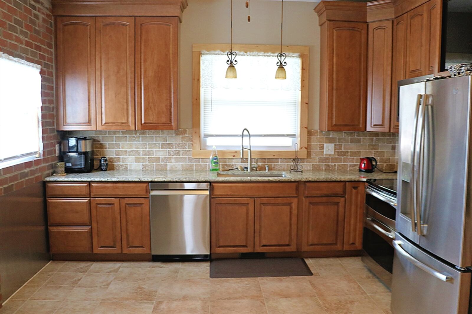 In the kitchen, exposed brick covers one wall and complements the brick backsplash. Appliances include a range, microwave, dishwasher and refrigerator.