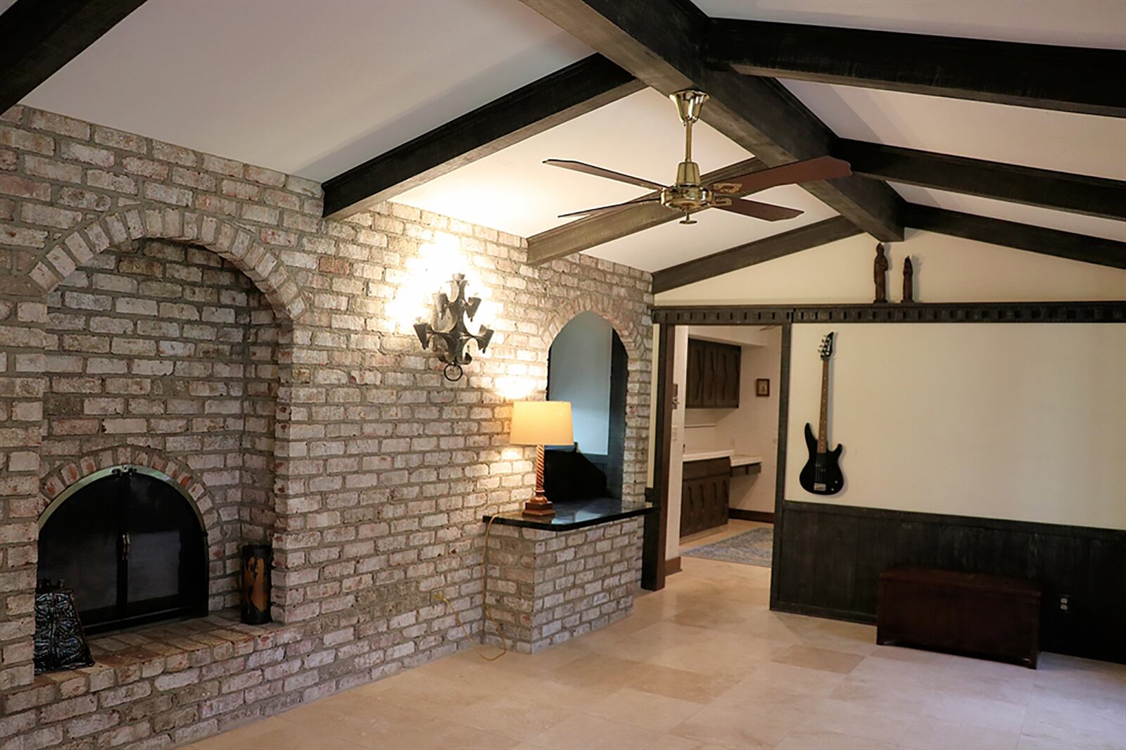 A slightly peaked ceiling is accented with wood cross beams and matching artwork railing completes the look of the tavern-style family room. Partial paneled walls match the rich wood tones and surround the tall windows. Distressed white brick covers one wall and has a double-arched fireplace with raised hearth. CONTRIBUTED PHOTO BY KATHY TYLER