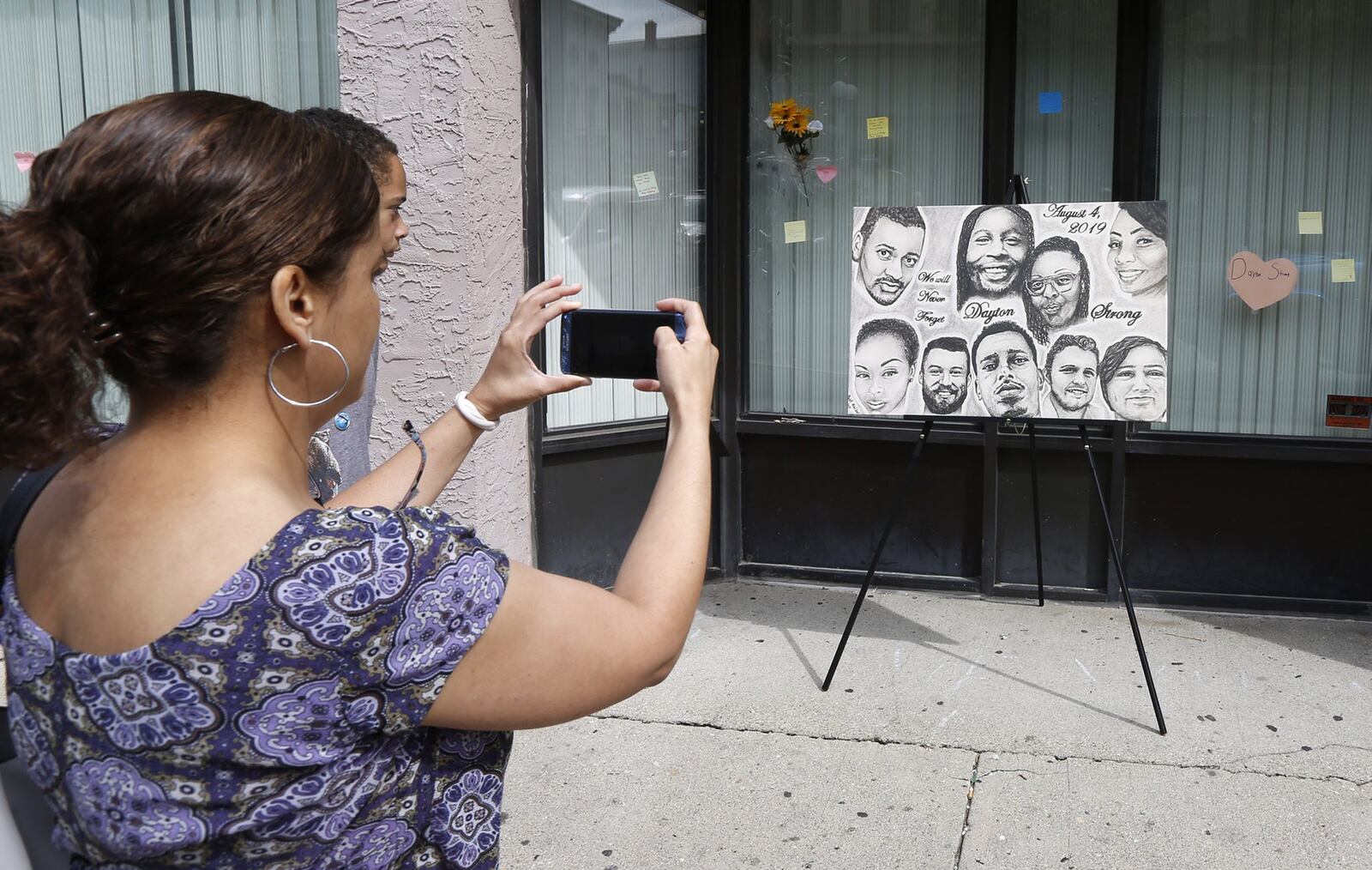 Native Daytonian Christi Colbert takes a picture of a new portrait that is on display in the Oregon District with the faces of the nine shooting victims painted by Abby Kaiser. Colbert was back in town from her current home in Maryland and visited East Fifth Street on Friday afternoon. TY GREENLEES / STAFF