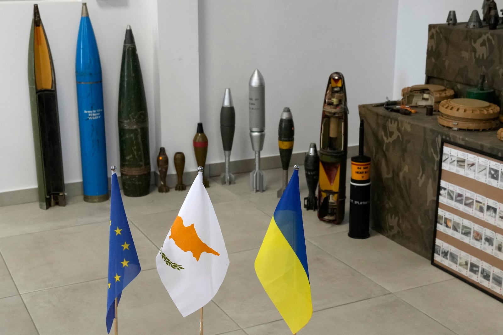 The flags of the European Union, Cyprus and Ukraine in front of a display of inert rockets, artillery shells and other munitions as part of a training course of Ukrainian personnel in the disposal of landmines and other explosive ordnance in Cyprus, at an army base in Nicosia, Thursday, Nov. 14, 2024. (AP Photo/Petros Karadjias)