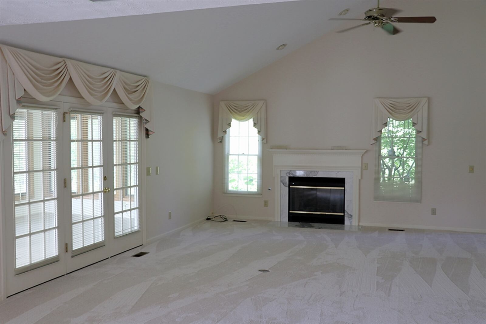 A gas fireplace has a marble hearth and dentil wooden mantel surround. The fireplace is flanked by windows. 