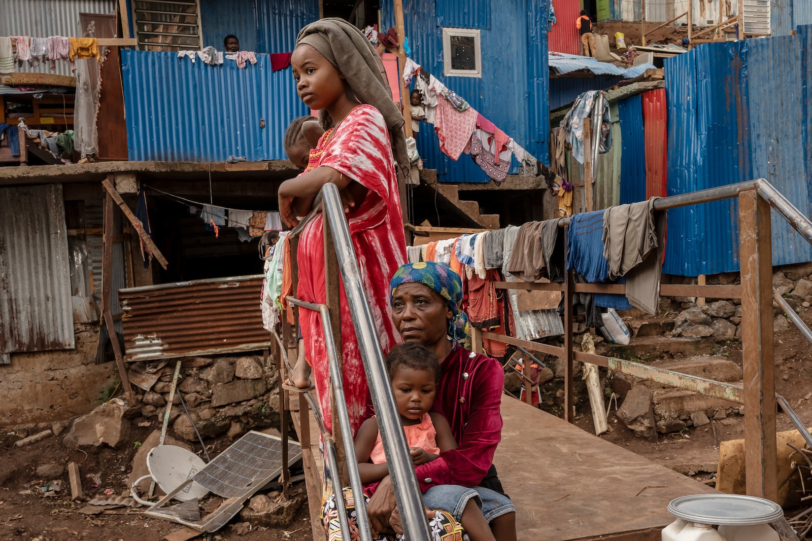 Women rest on a footbridge over a stream filled with debris in the Kaweni slum in the French Indian Ocean island of Mayotte, Thursday, Dec. 19, 2024, after Cyclone Chido. (AP Photo/Adrienne Surprenant)