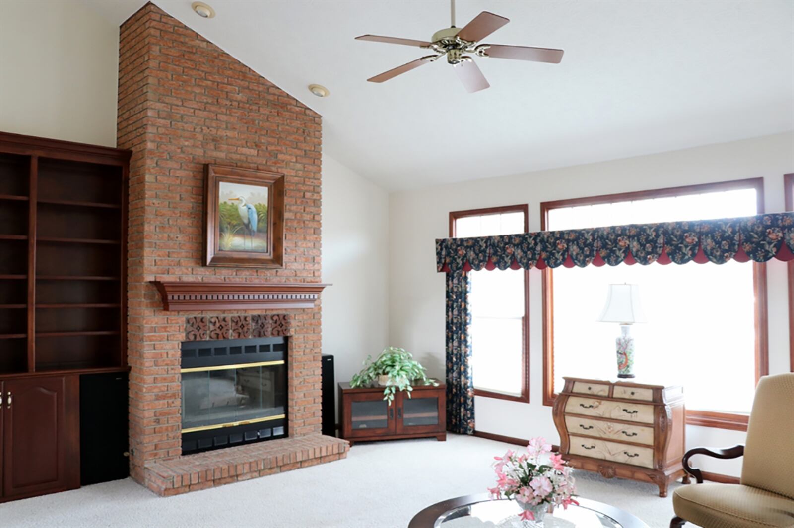 A cathedral ceiling peaks above the great room, which has a wall of windows that look out over the back yard. A brick fireplace has detailed brick accents, a brick hearth and a wood-beam mantel. A built-in bookcase with cabinets is next to the fireplace. CONTRIBUTED PHOTO BY KATHY TYLER