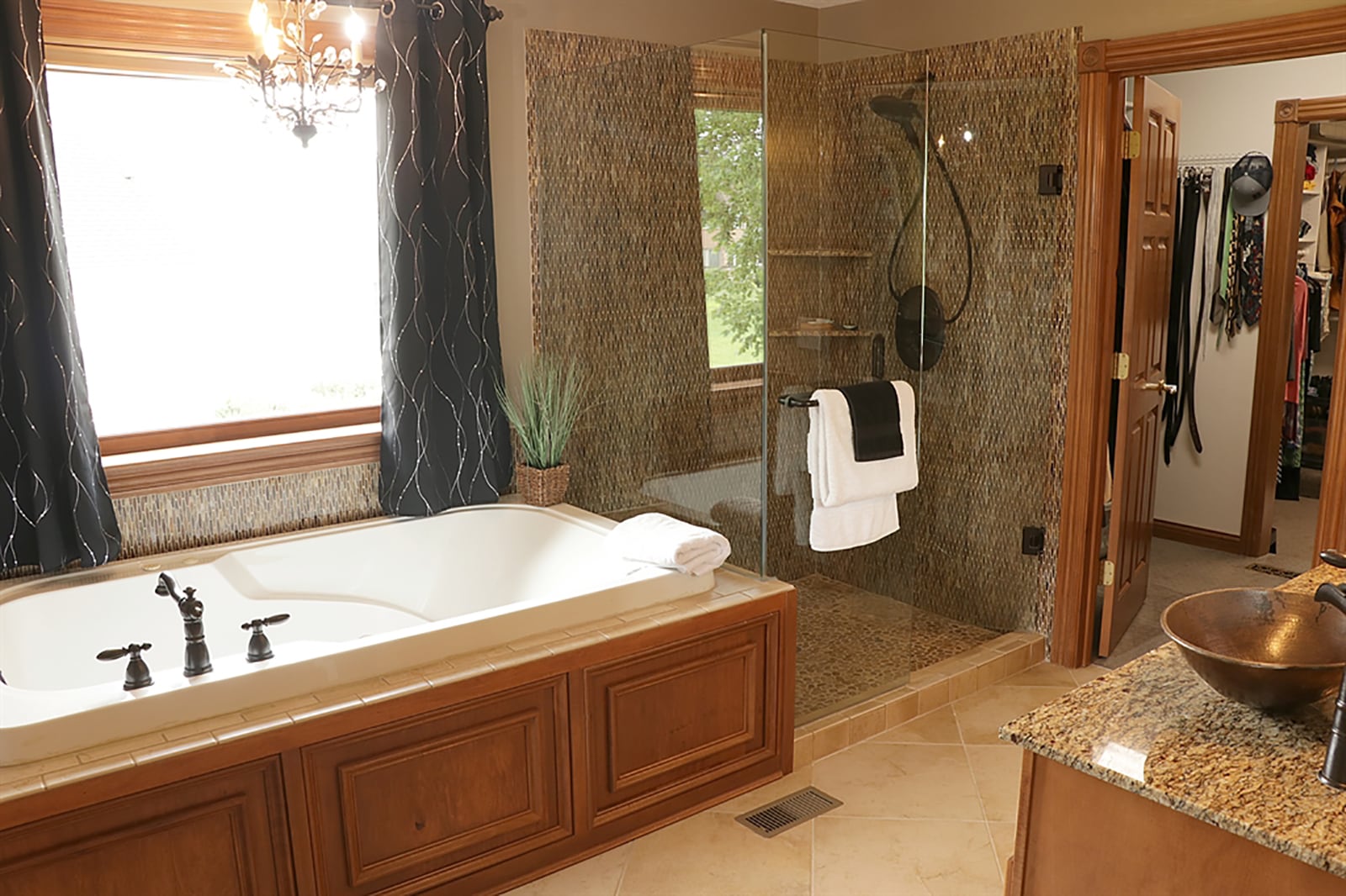 The main bedroom suite’s bath features a whirlpool tub below a window and chandelier.  A walk-in shower has river-stone flooring and ceramic-tile surround with glass doors. CONTRIBUTED PHOTO BY KATHY TYLER