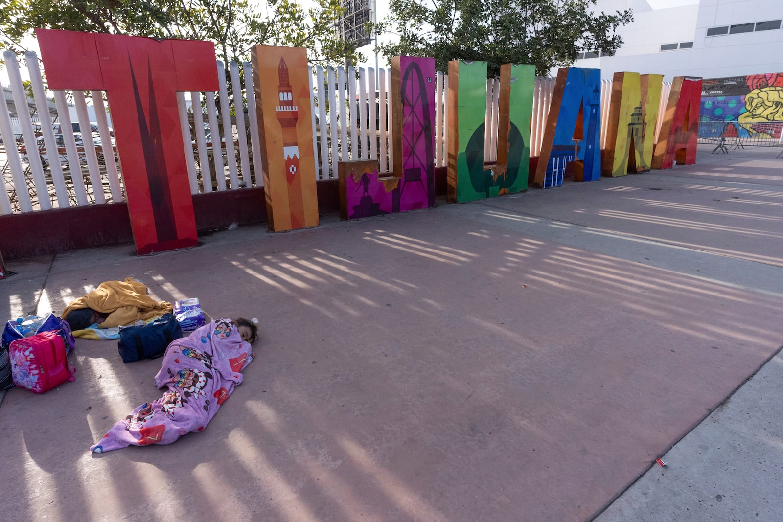 A girl from the Mexican state of Morelia sleeps in front of a sign for Tijuana as her family's CBP One application appointments to apply for asylum in the United States were declared not valid on the application Monday, Jan. 20, 2025, in Tijuana, Mexico, shortly after President Donald Trump was sworn-in. (AP Photo/Gregory Bull)